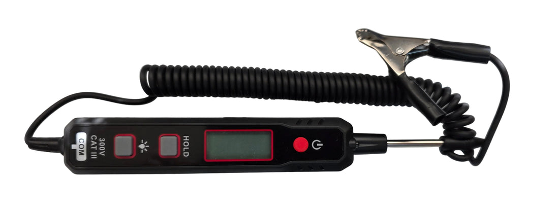 A handheld digital voltmeter with a coiled cord and metal clip, shown with its black retail box, a small battery, and a paper manual on a light reflective surface.