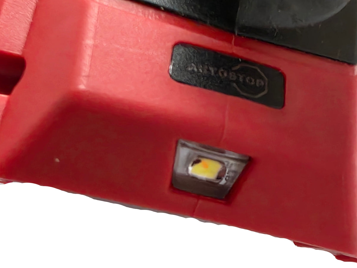 Close-up of a red AUTO STOP branded plastic housing with a small illuminated LED light and a black brand label.