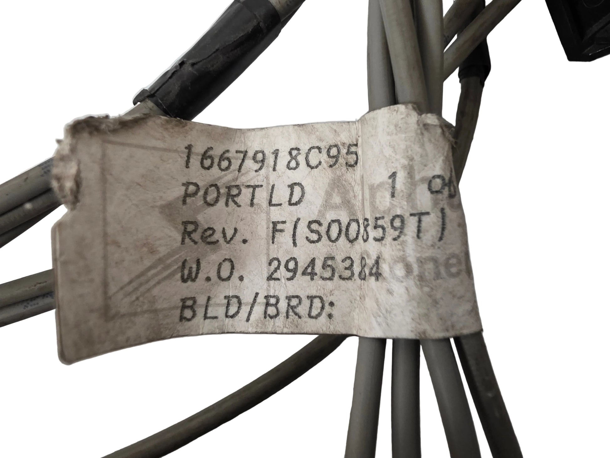 A close-up of a used paper label attached to gray and black cables, printed with a part number '1667918C95' and other manufacturing details.