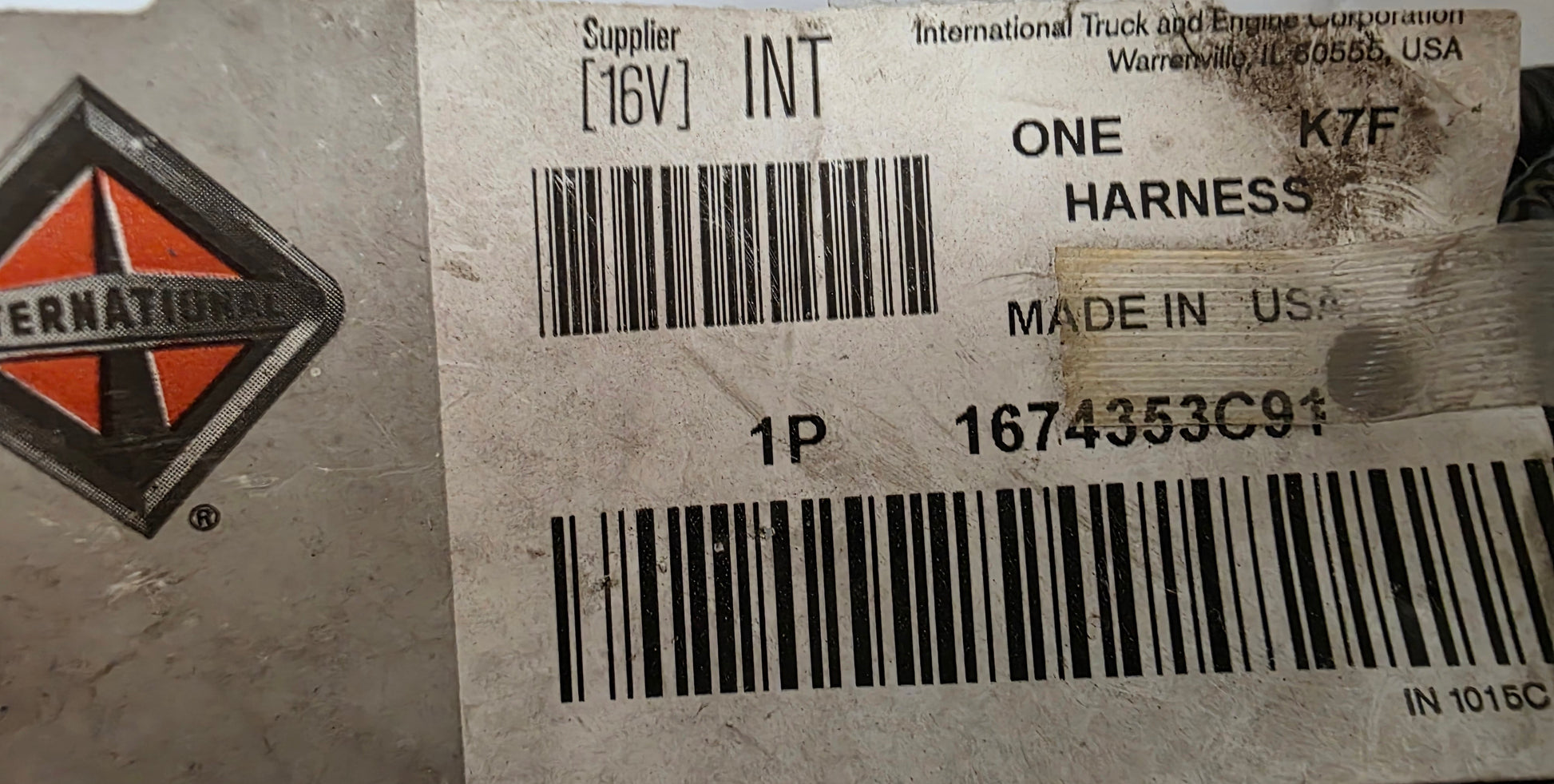 A close-up of a used International truck and engine harness with its original paper label. The label shows the International logo, part number 1674353C91, and specifies it is a one-pin black harness for a 16V system.